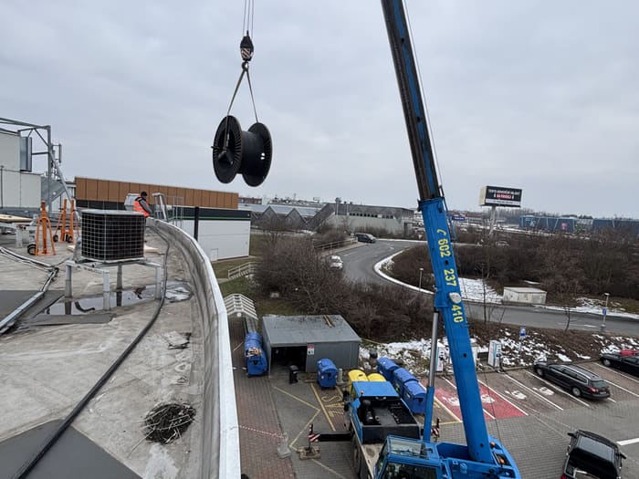 Mobile crane lifting a cable drum onto the roof of the building