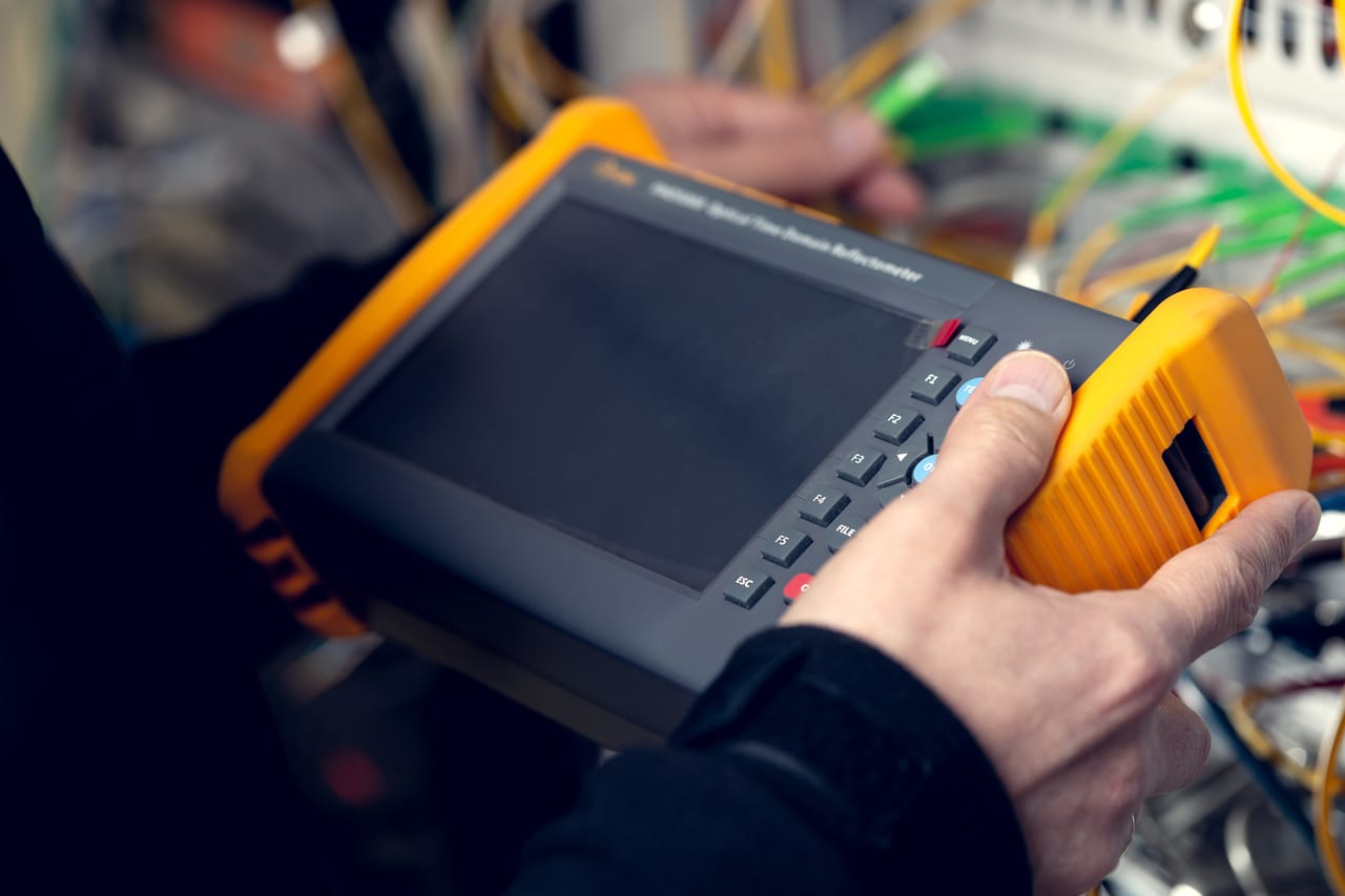 Technician holding an OTDR in front of an optical distribution frame